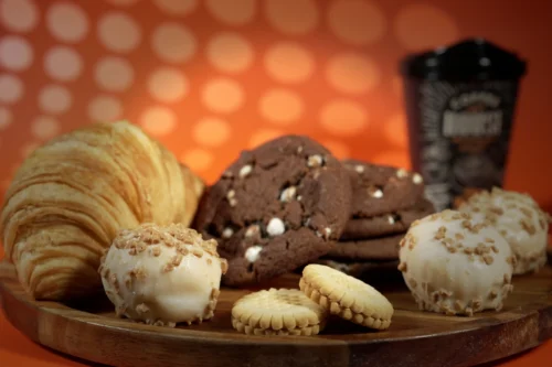 A wooden platter displaying various baked goods, including croissants, cookies, and decorative pastries, against an orange backdrop.