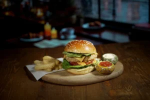 Delicious gourmet burger with cheese, lettuce, and tomato, served with golden fries and a side of dipping sauce.