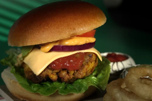 Juicy burger with cheese, lettuce, tomato, and onion, served with onion rings on the side. Perfect for food photography.
