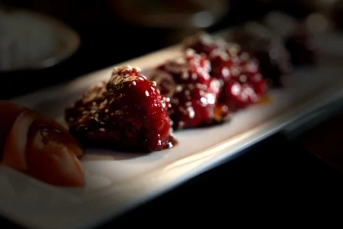 Close-up of glistening red sauce-coated food on a white plate, showcasing enticing food photography for commercial use.