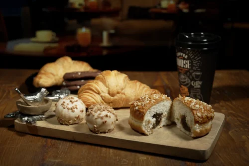 Assorted pastries including croissants, doughnuts, and a coffee cup on a wooden platter, showcasing food photography expertise.