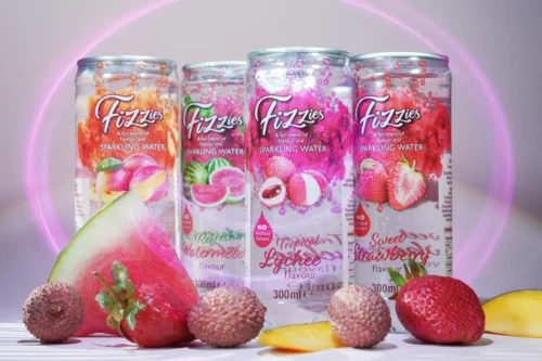 Fizzies sparkling water cans with various fruit flavours, including watermelon and lychee, arranged with fresh fruit.