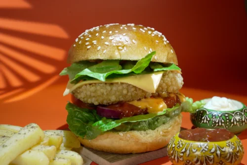 Succulent cheeseburger with lettuce, tomato, and sauces, set against a vibrant orange backdrop, ideal for food photography.