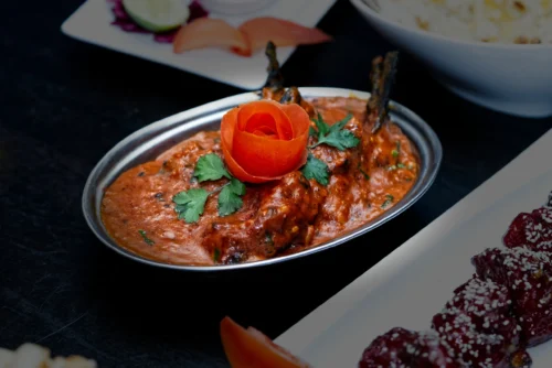 A beautifully presented dish of meat in a rich sauce, garnished with a rose made of carrot and fresh coriander.