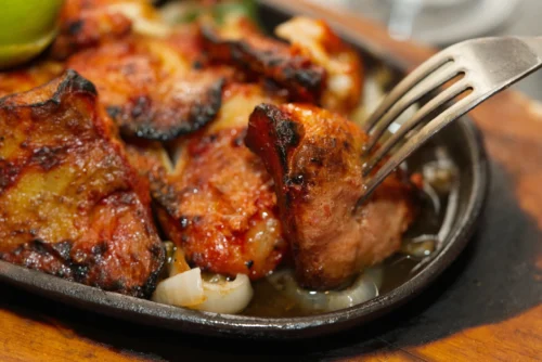 Sizzling grilled chicken on a hot plate with garnish, showcasing food photography for culinary promotion.