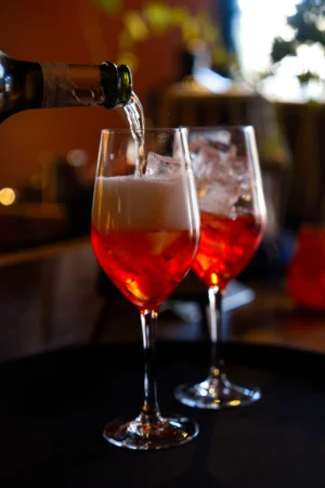 Two glasses filled with red cocktails and ice, with one being poured from an unseen bottle, showcasing vibrant food photography.