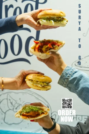 Four hands holding vibrant, gourmet food bun offerings in front of a menu backdrop with a "ORDER NOW" QR code.
