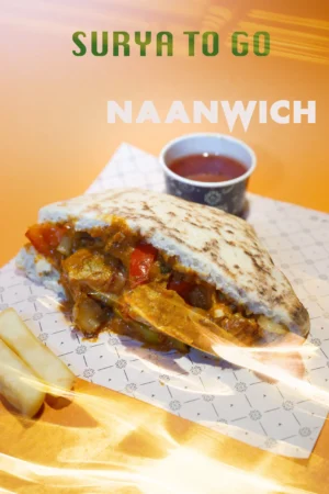 Naanwich filled with vibrant vegetables and curry, served with fries and dipping sauce, against a warm orange backdrop.