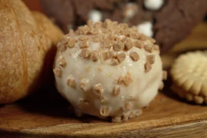 Decadent dessert with a creamy coating and crunchy bits, surrounded by cookies and pastries on a wooden platter.